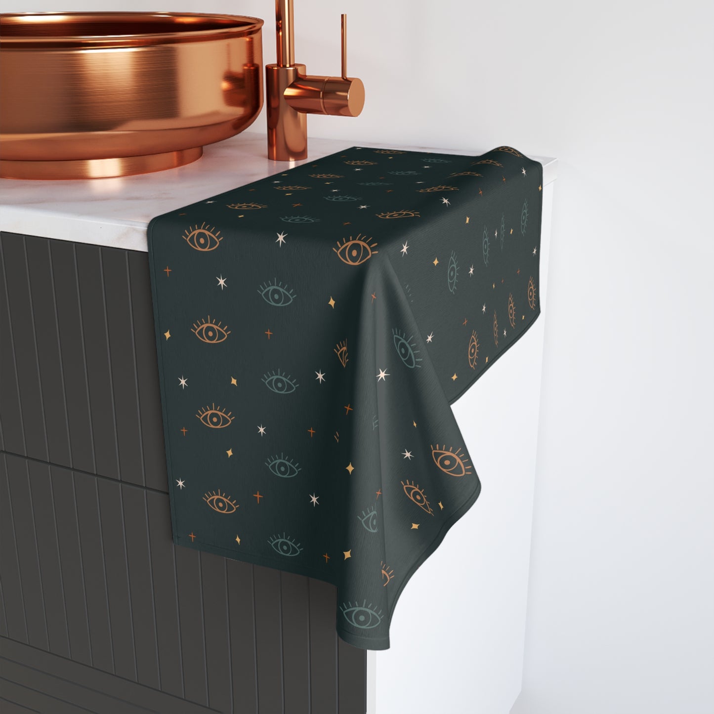 Dark green towel with eye pattern draped over a black cabinet with copper fixtures.
