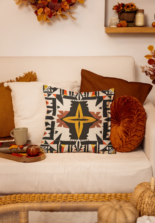Geometric throw pillow on cream couch with fall decor and autumn leaves