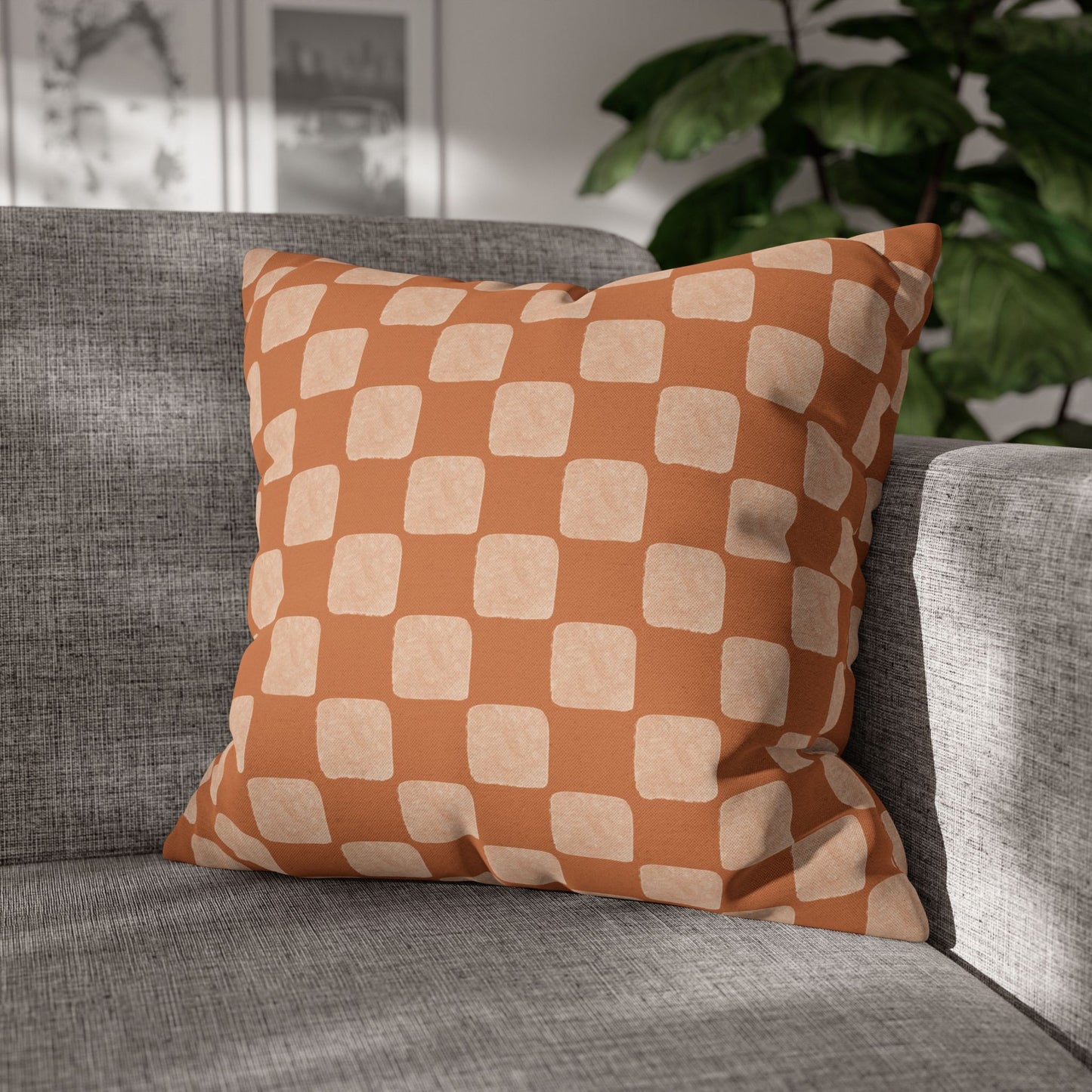 Checkered orange and beige pillow on a gray sofa with a plant in the background