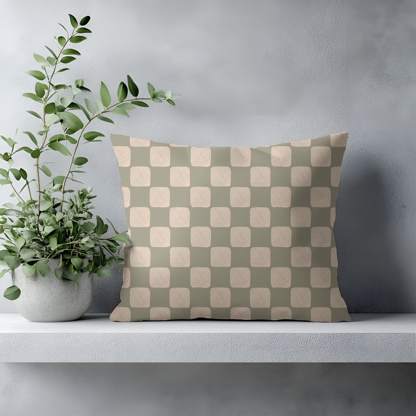 Checkered pillow with green and beige pattern on a gray surface next to a potted plant.