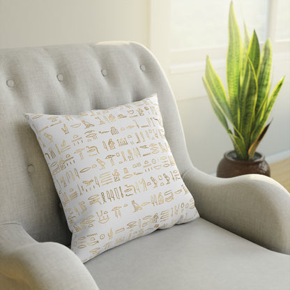 A throw pillow with a gold pattern of Egyptian hieroglyphics on a cream-colored armchair.
