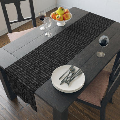 A black table runner with a geometric pattern laid out on a dining table with dishes and a floral centerpiece.