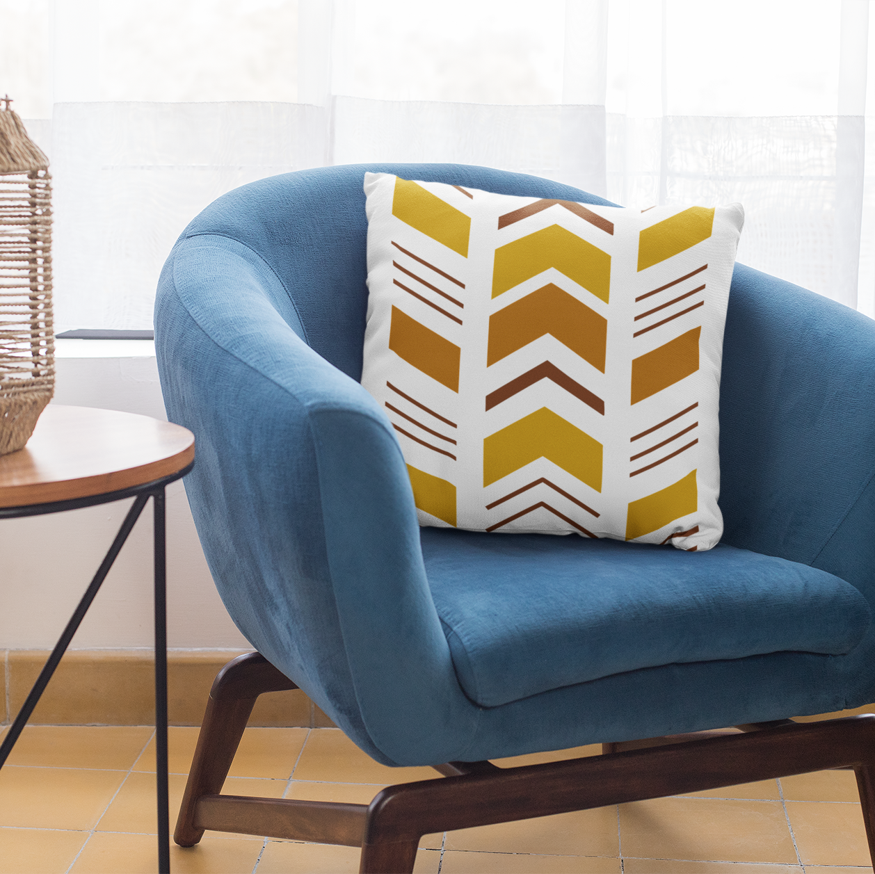 Blue armchair with a Mudcloth patterned pillow next to a side table with a woven lantern, in a bright room.