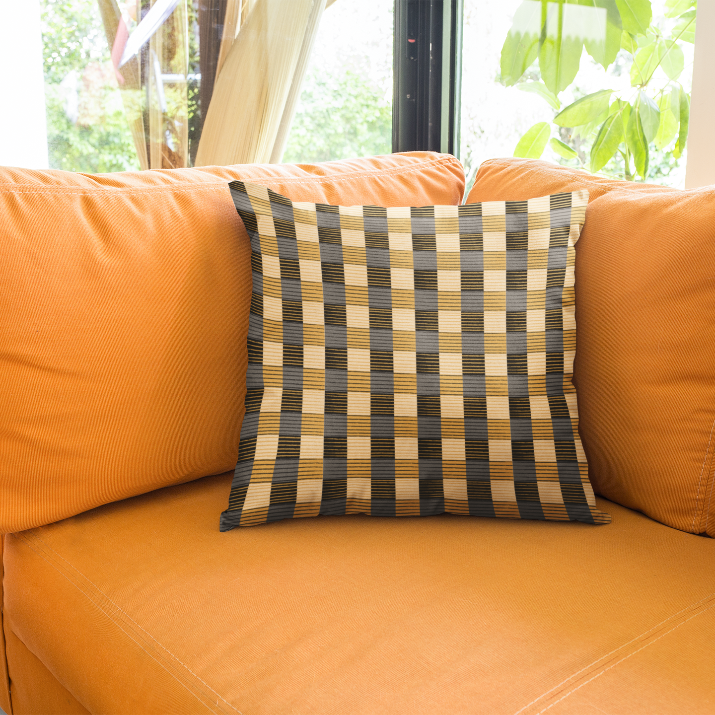 Orange sofa with a plaid pillow in a room with windows and greenery outside