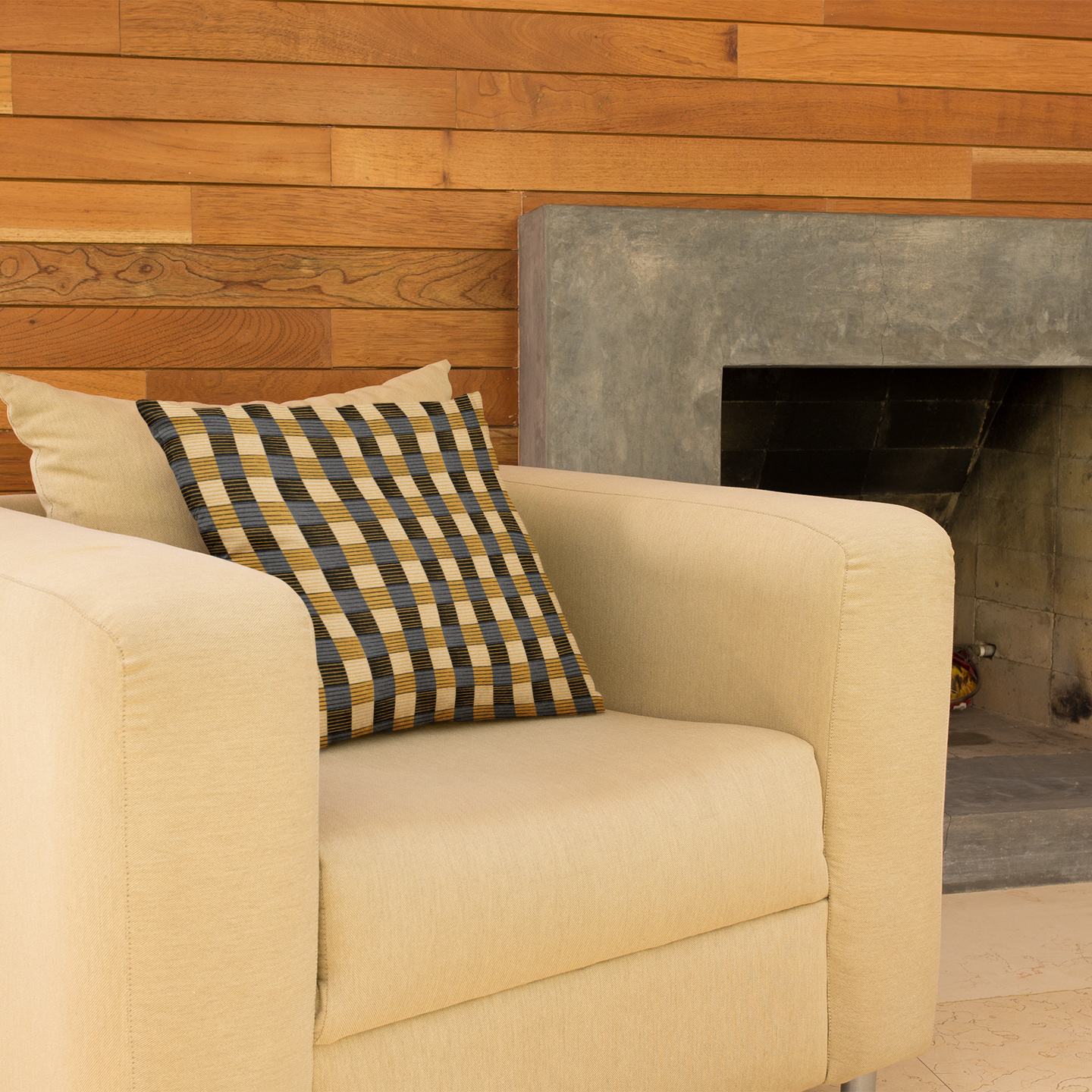 Beige armchair with a checkered pillow in front of a stone fireplace.