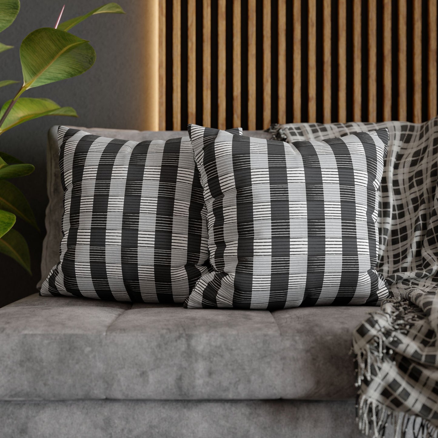 Two square throw pillows with a striped African Plaid pattern in beige and black colors, placed on a gray sofa.