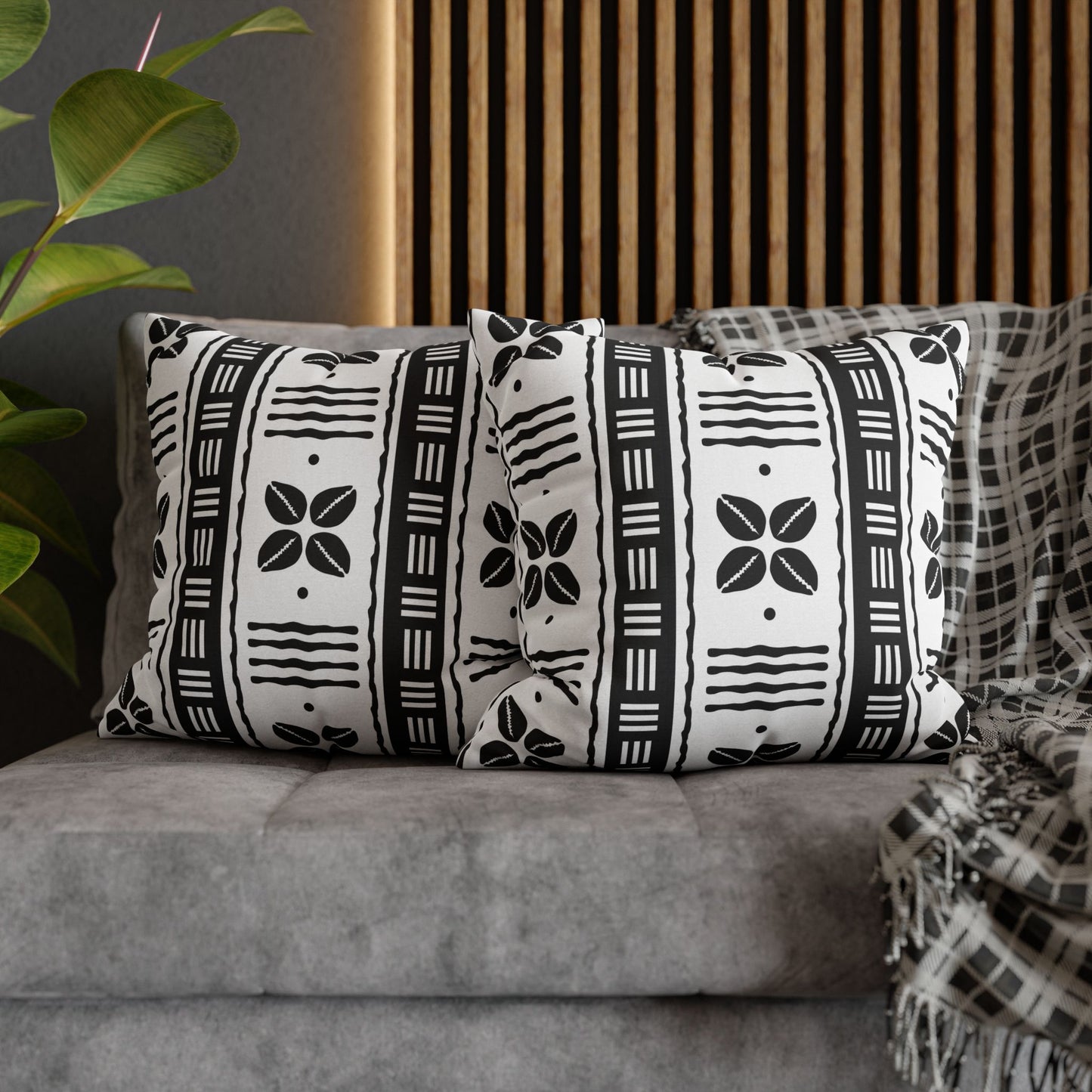 Two square pillow covers with a white African shells and mudcloth pattern on a grey sofa.
