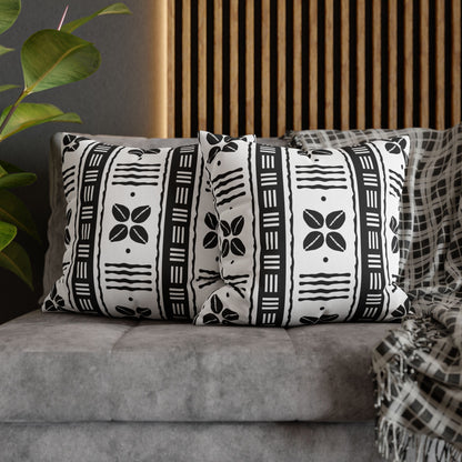 Two square pillow covers with a white African shells and mudcloth pattern on a grey sofa.