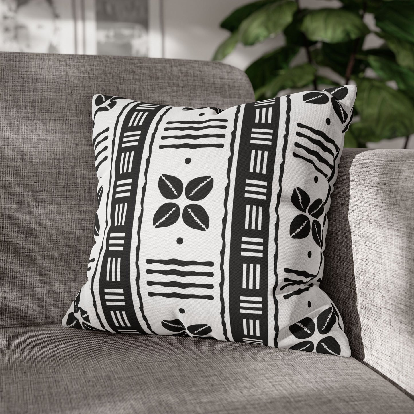Two square pillow covers with a white African shells and mudcloth pattern on a grey sofa.