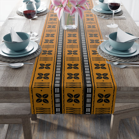 A decorative table runner with African shells and tribal print in black, yellow, and white, displayed on a dining table.