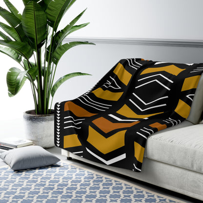 Black and yellow patterned blanket draped over a sofa in a living room setting with a plant and rug.