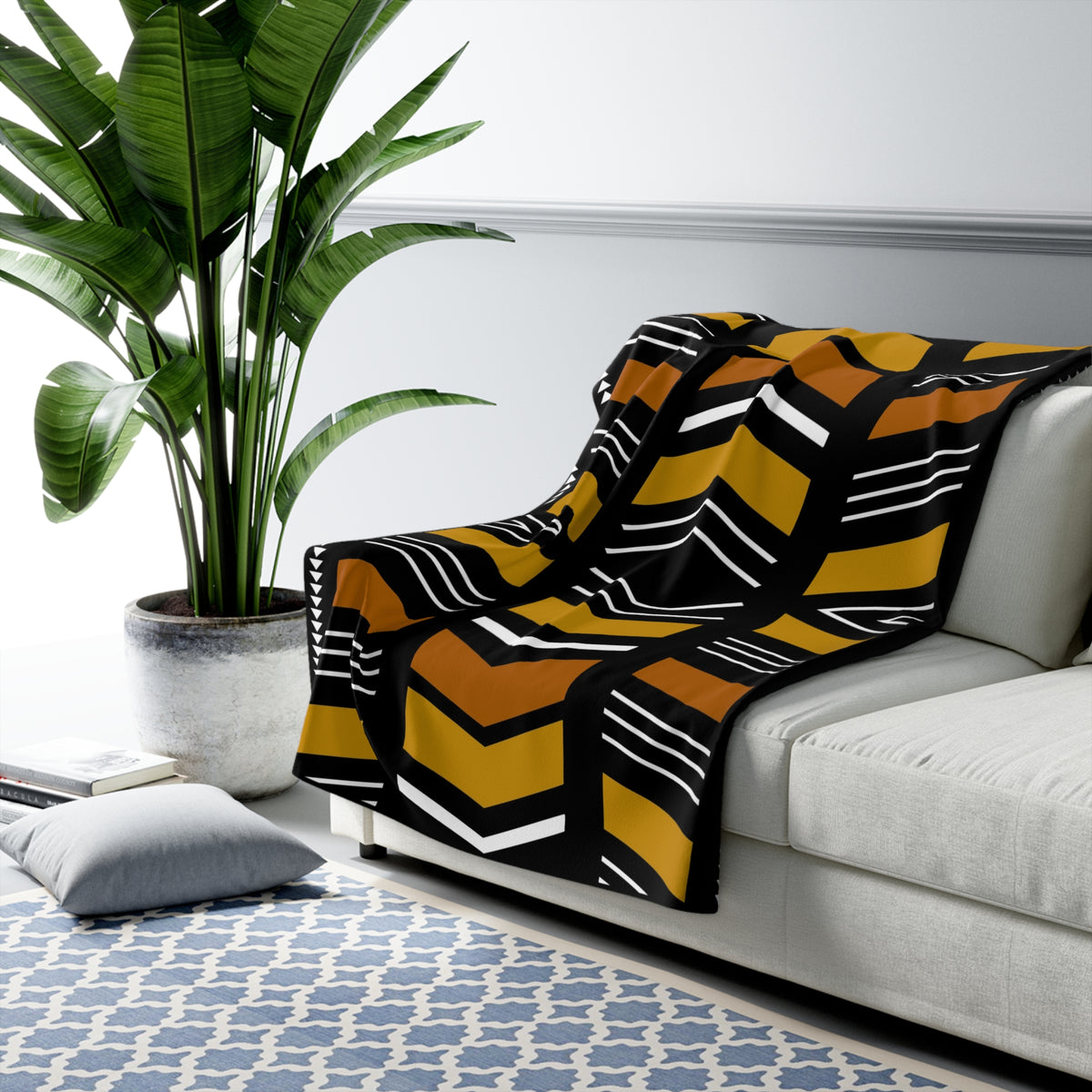 Patterned blanket draped over a sofa in a living room with a plant and rug.