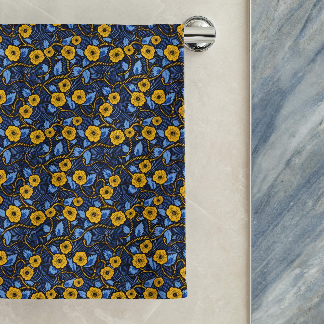 Towel with yellow floral pattern hanging on a rack against a marble wall.