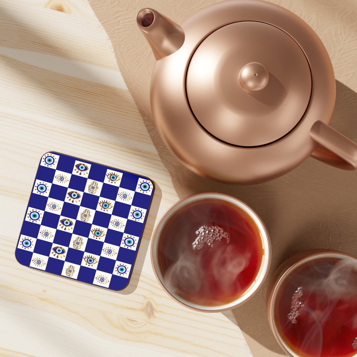 Teapot and cups of tea on a wooden surface with a decorative coaster.