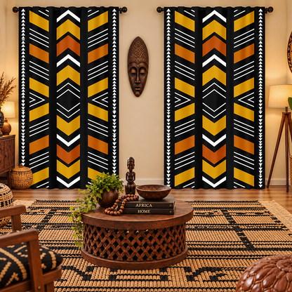 A pair of tall window curtains with a bold African-inspired geometric pattern in black, mustard yellow, orange, and white, hanging in a styled living room setting.