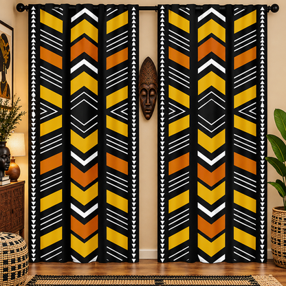 A pair of floor-length curtains hanging in a room, featuring a bold African-inspired geometric pattern with vertical stripes of yellow, orange, black, and white chevrons and triangles. The curtains are styled in a warm room setting with a wooden mask on the wall, plants, and a woven rug.