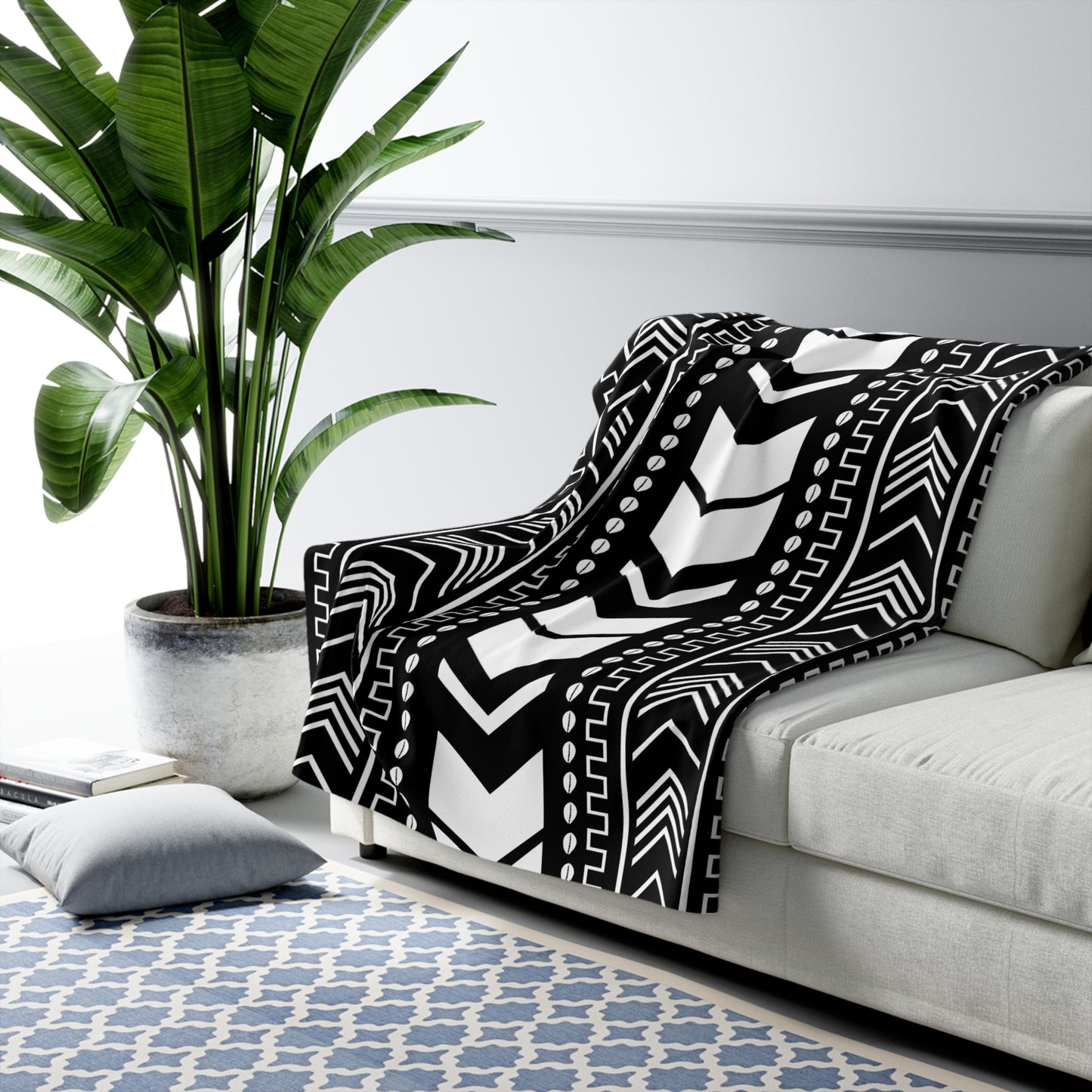 Black and white patterned throw blanket on a gray sofa with a plant and rug in the background
