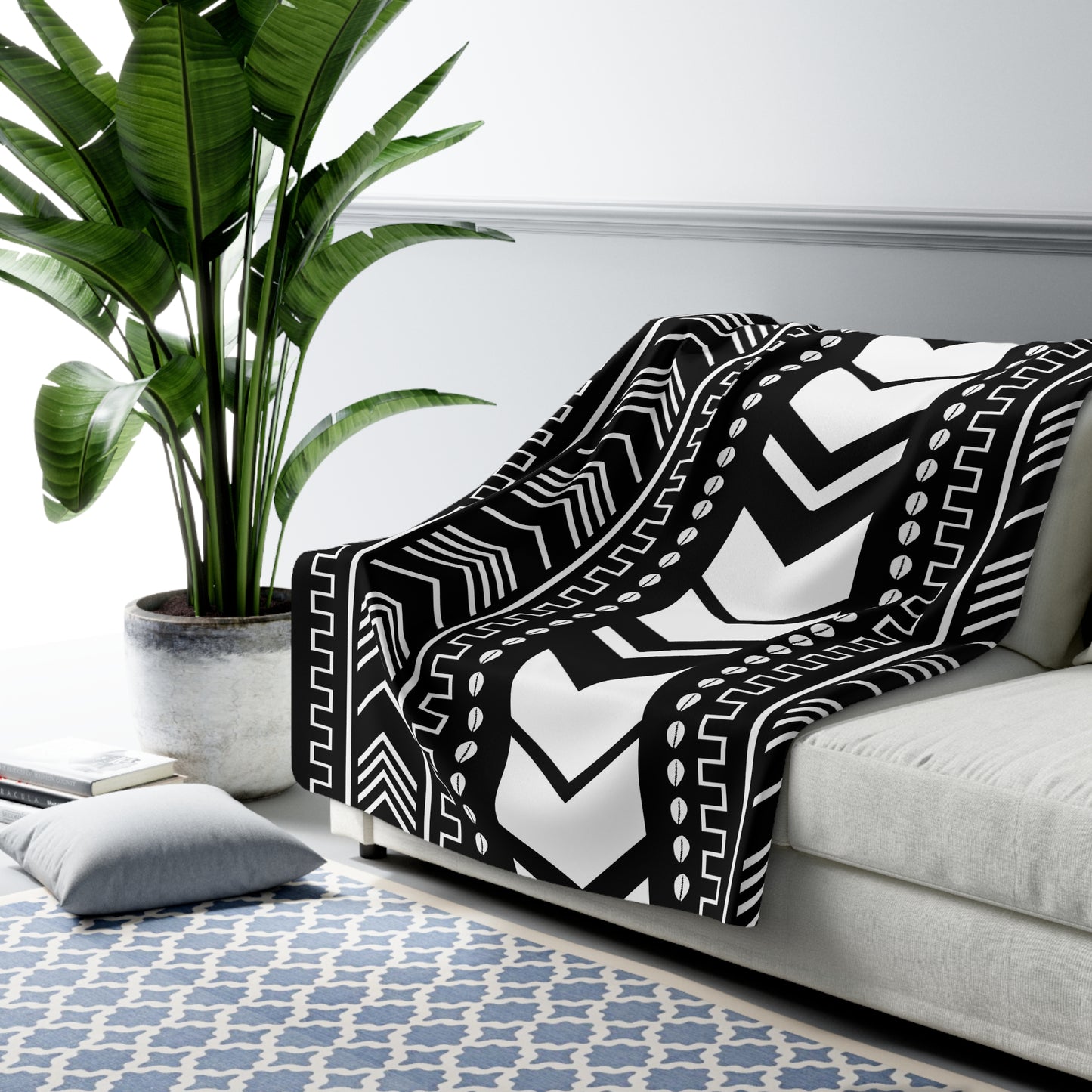 Black and white patterned throw blanket draped over a sofa in a living room with a plant and rug.