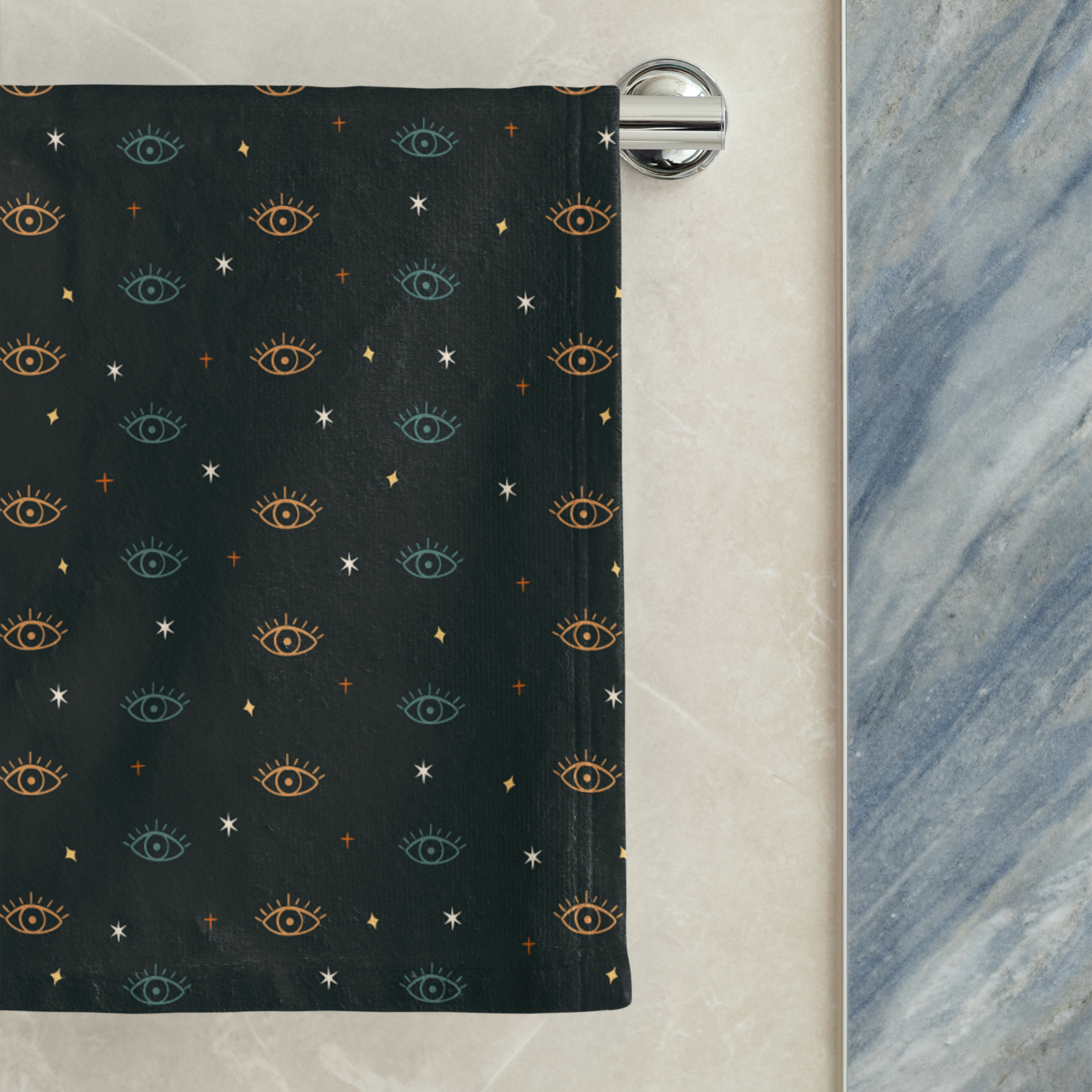 Black towel with eye pattern hanging on a rack against a marble wall.