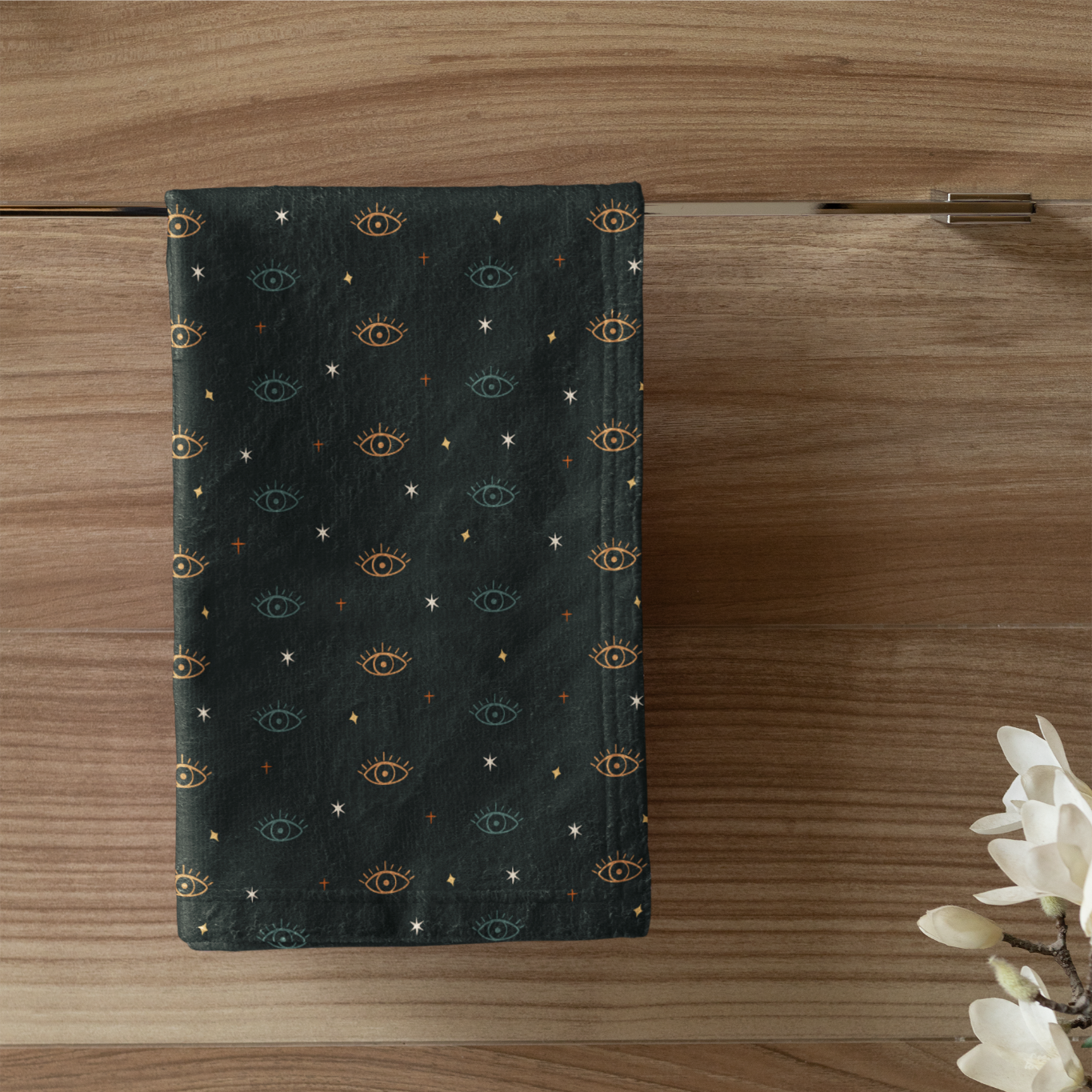 Dark green towel with gold patterns hanging on a wooden door, next to a white candle in a green holder.