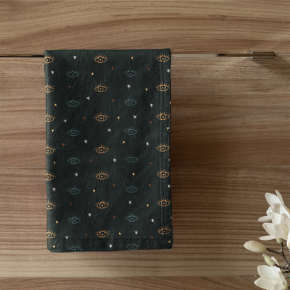 Dark green towel with gold patterns hanging on a wooden door, next to a white candle in a green holder.
