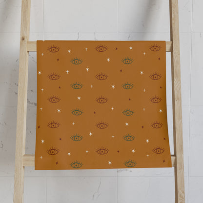 Gold towel with eye pattern on a wooden ladder against a white wall
