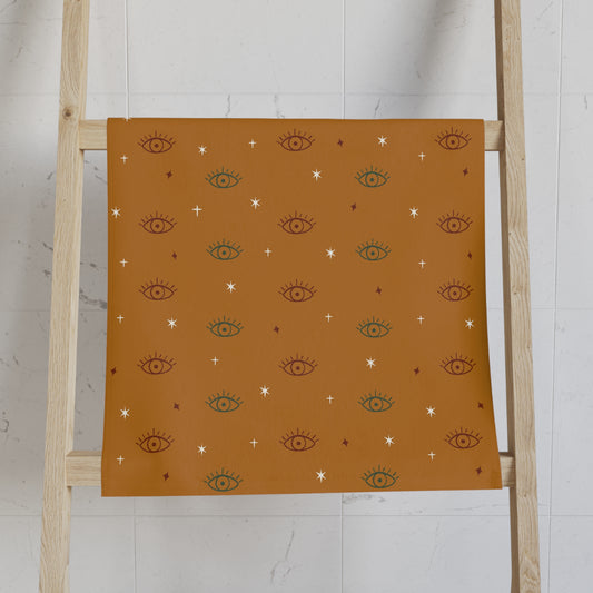 Gold towel with eye pattern on a wooden ladder against a white wall
