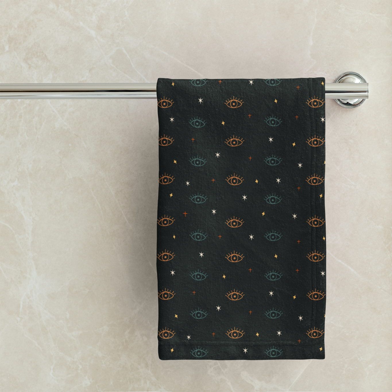 Green towel with eye pattern hanging on a towel rack against a marble wall.