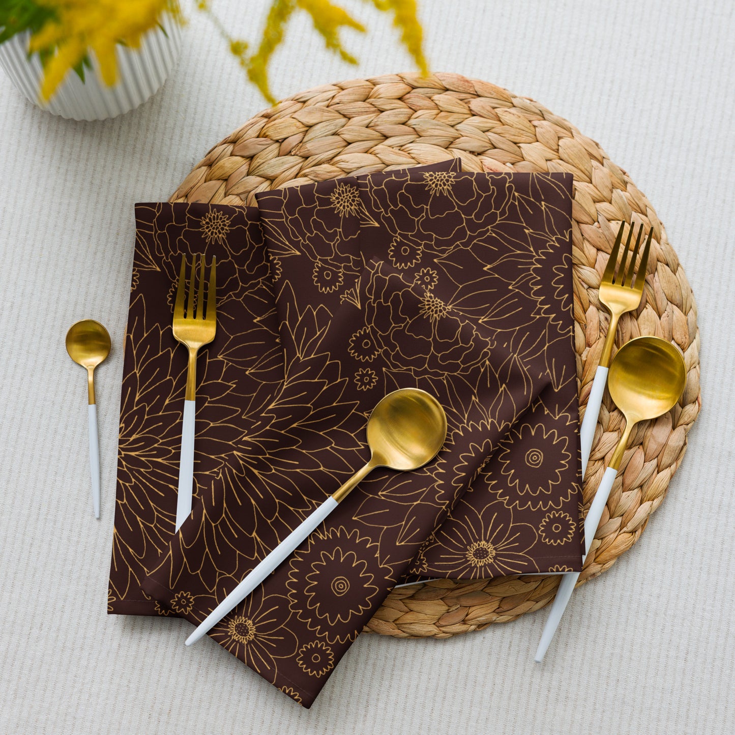 Brown floral-patterned napkin with gold cutlery on a woven placemat.