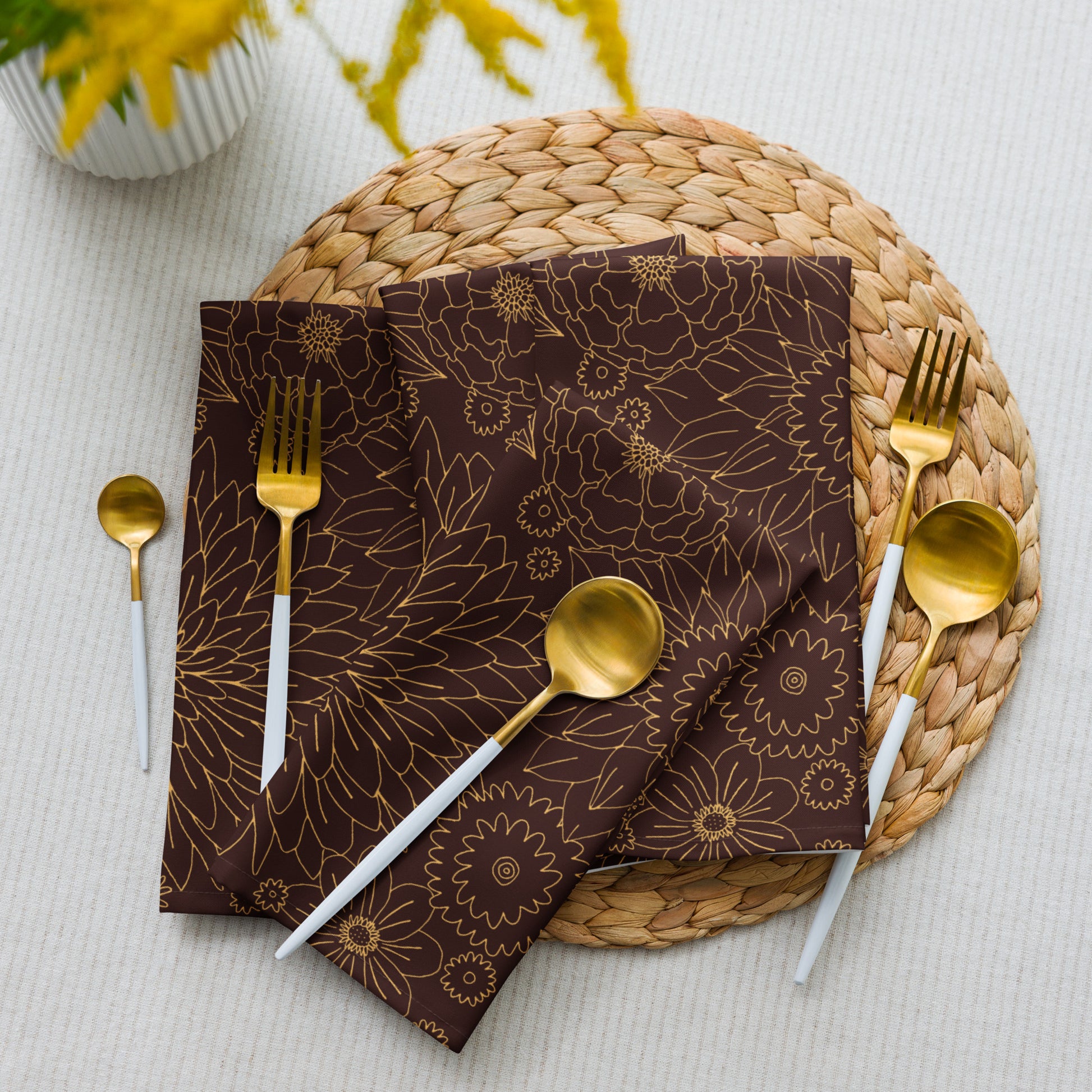 Brown floral-patterned napkin with gold cutlery on a woven placemat.