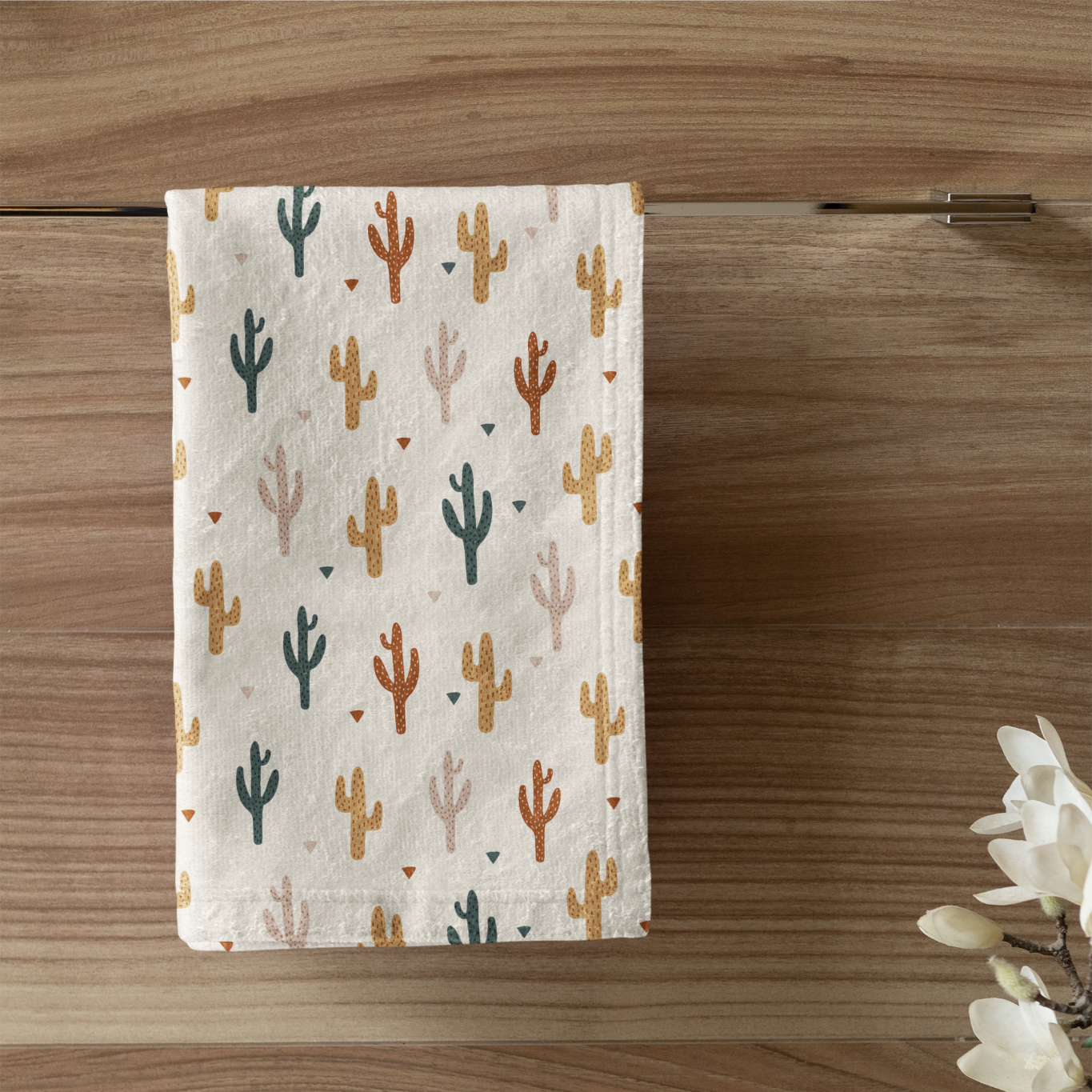 Towel with cactus pattern hanging on a wooden wall next to a candle and plant.