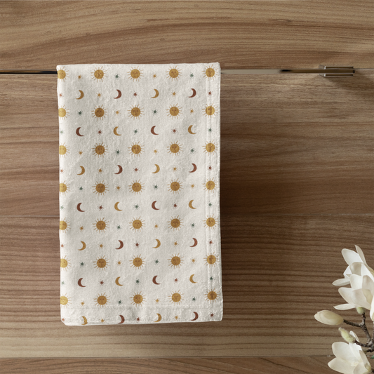 Towel with moon phase pattern hanging on a wooden wall above a toilet with a candle and plant.