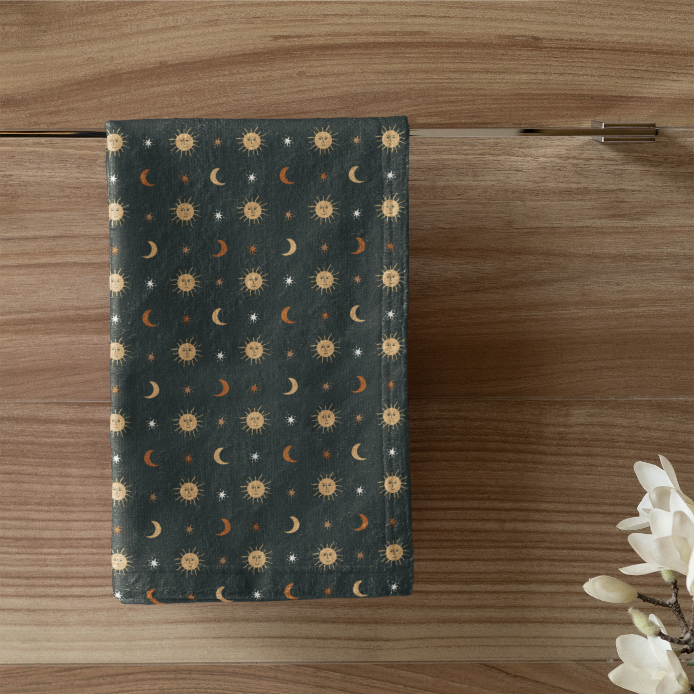 Towel with celestial pattern hanging on a wooden wall next to a white candle in a green holder.