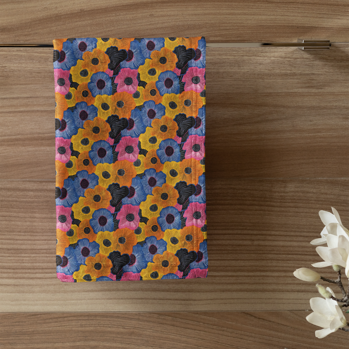 Colorful floral patterned towel hanging on a wooden door with a candle and plant in the foreground.