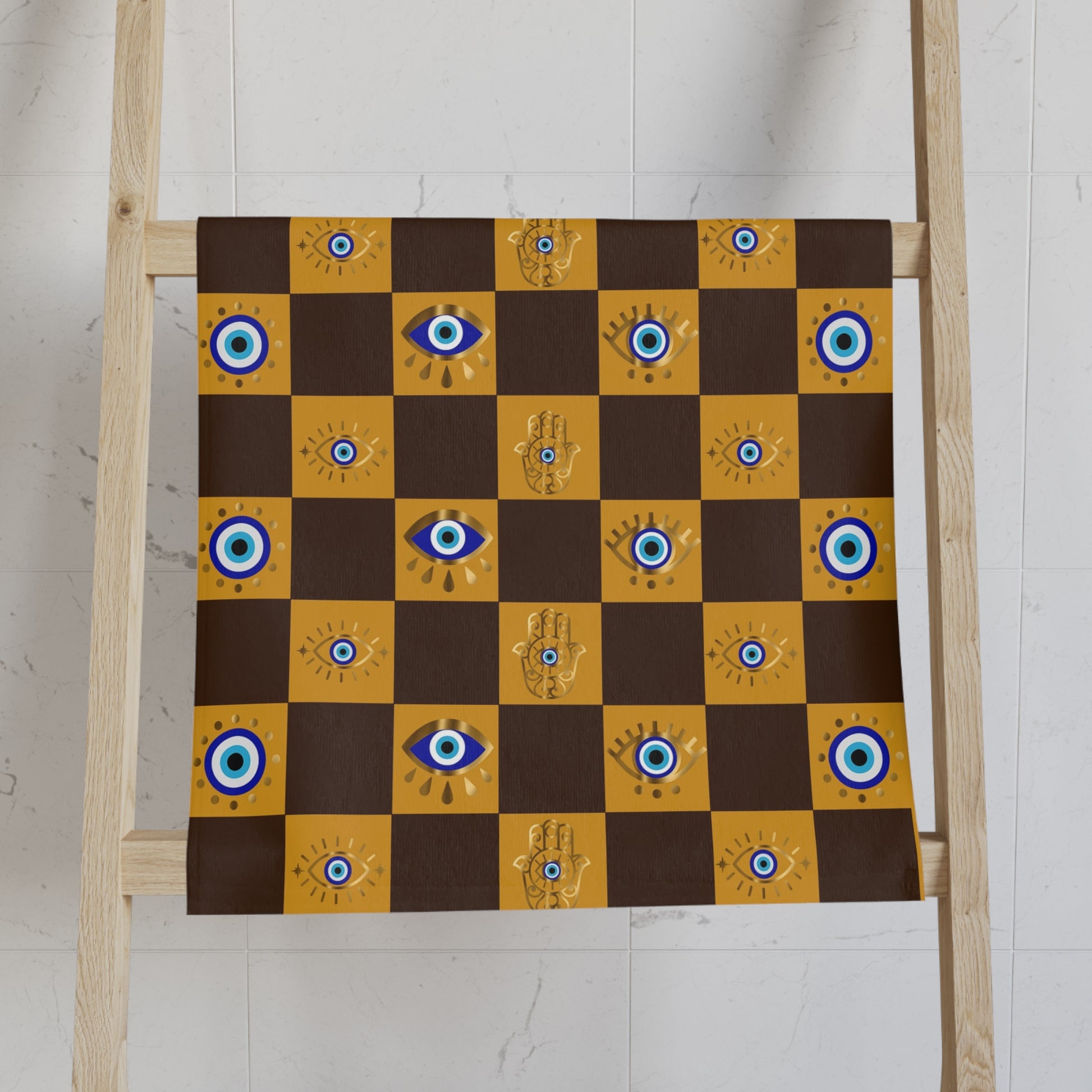 Checkered cloth towel with eye and hand designs on a wooden ladder against a white wall.