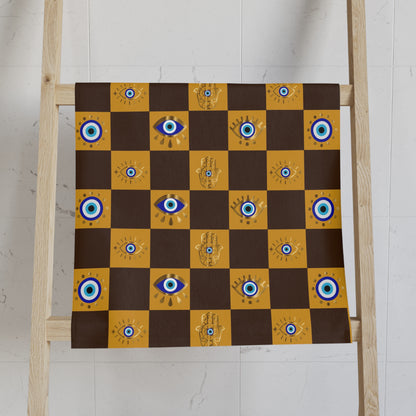 Checkered cloth towel with eye and hand designs on a wooden ladder against a white wall.