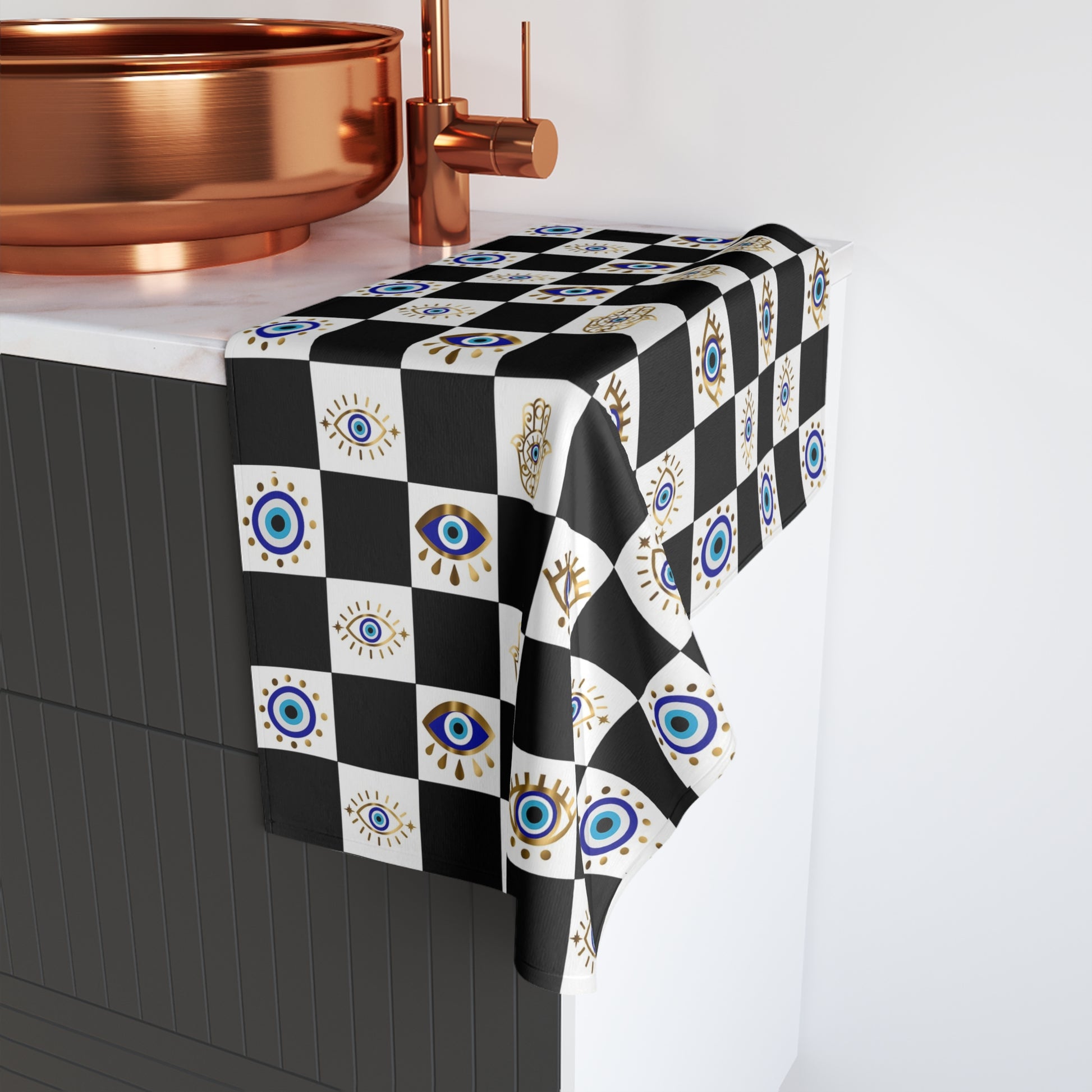 Checkered hand towel with eye pattern on a kitchen counter with copper fixtures.