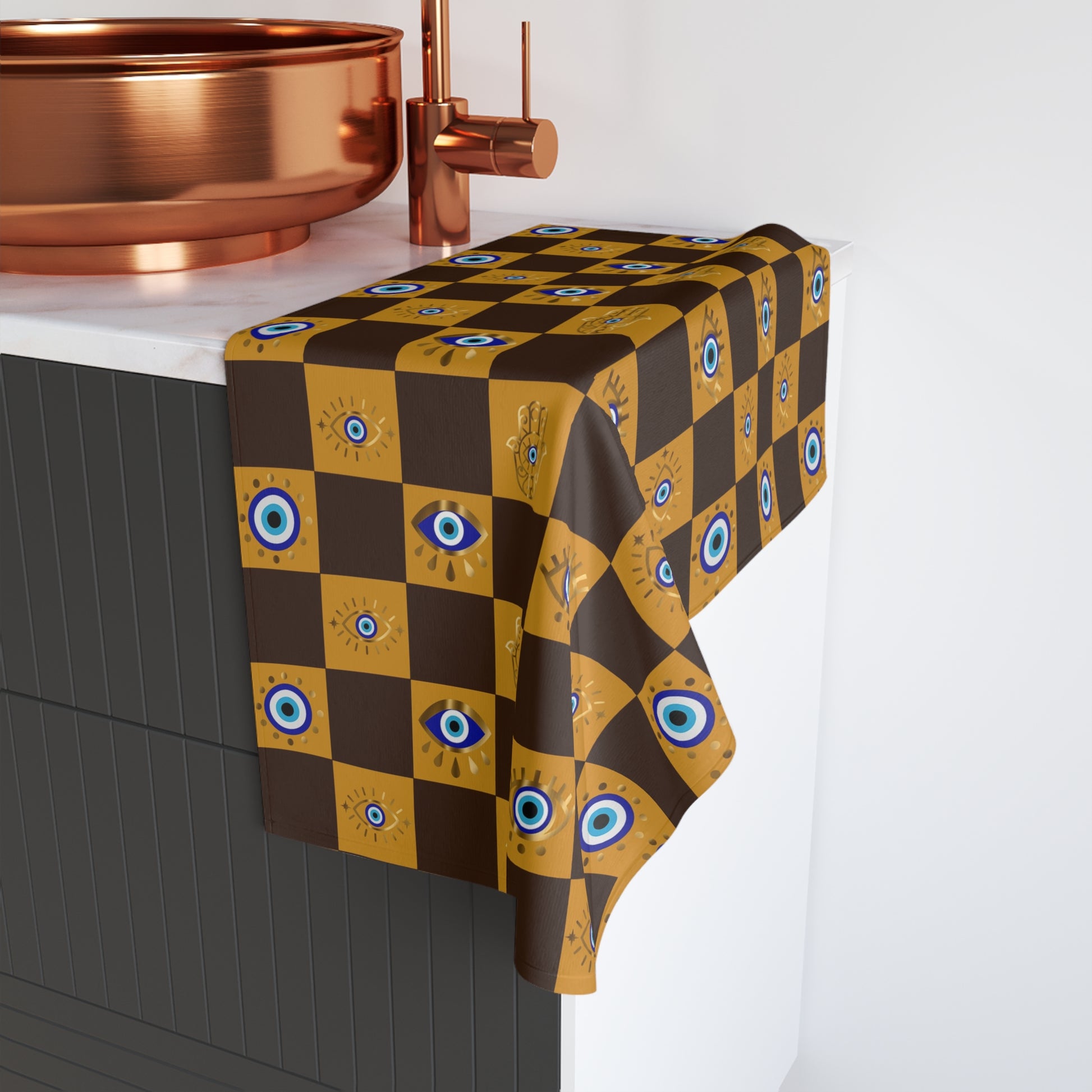 Checkered hand towel with eye pattern draped over a table next to a copper sink.