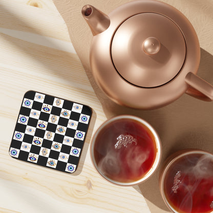 Rose gold teapot with two cups of tea on a checkered evil eye hamsa coaster set.