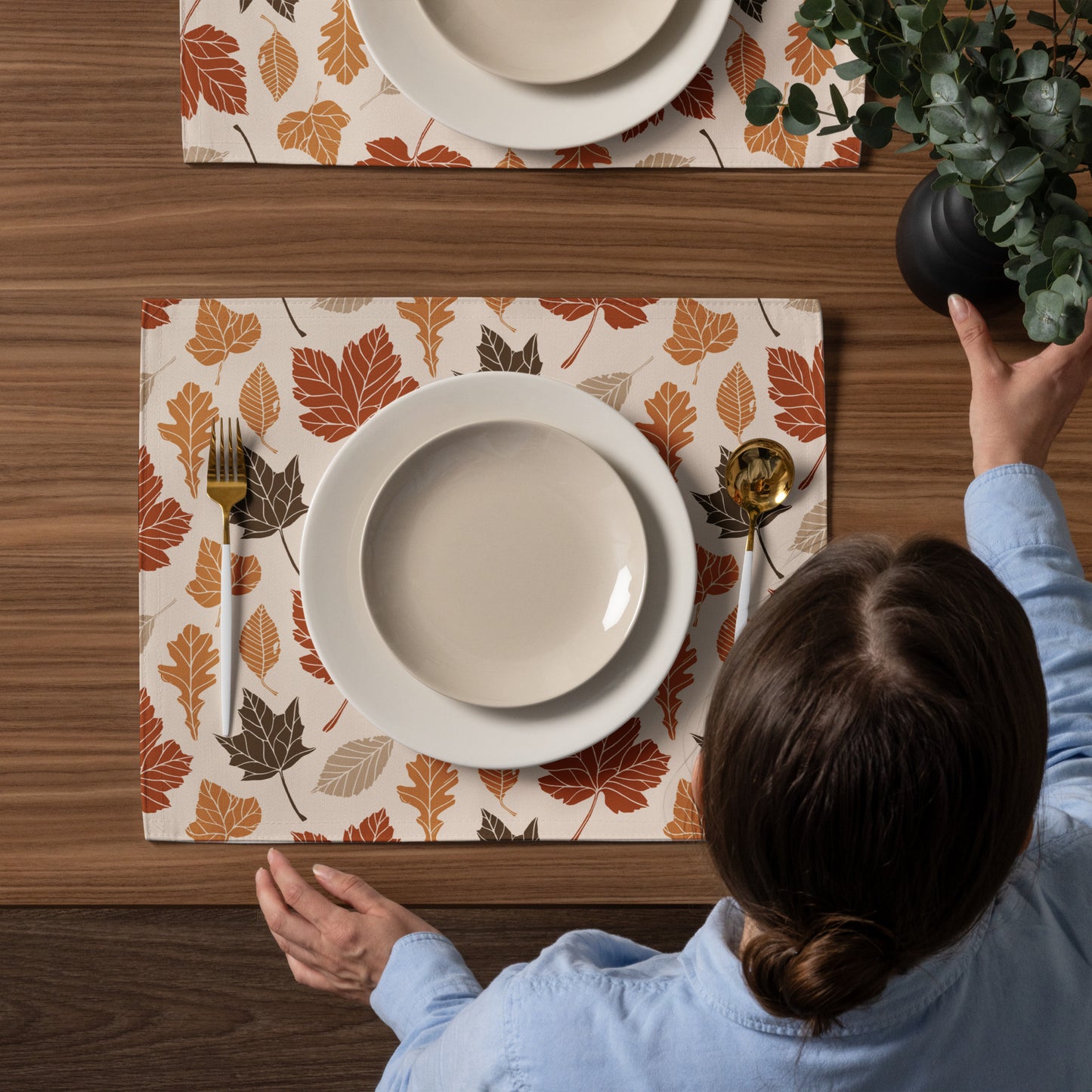 Person setting a table with fall-themed placemats and dinnerware.