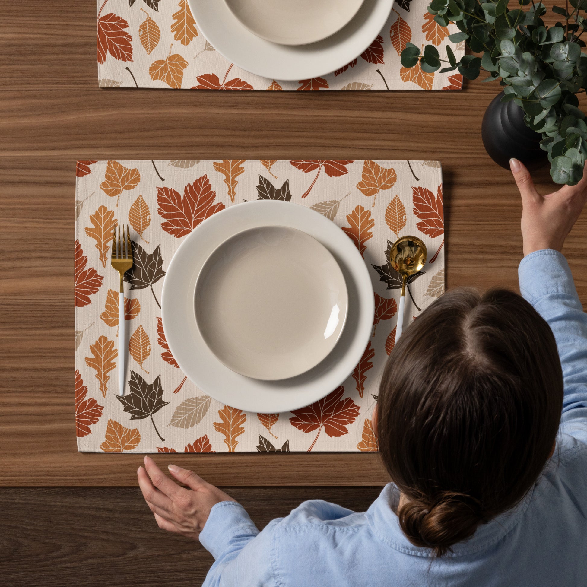 Person setting a table with fall-themed placemats and dinnerware.