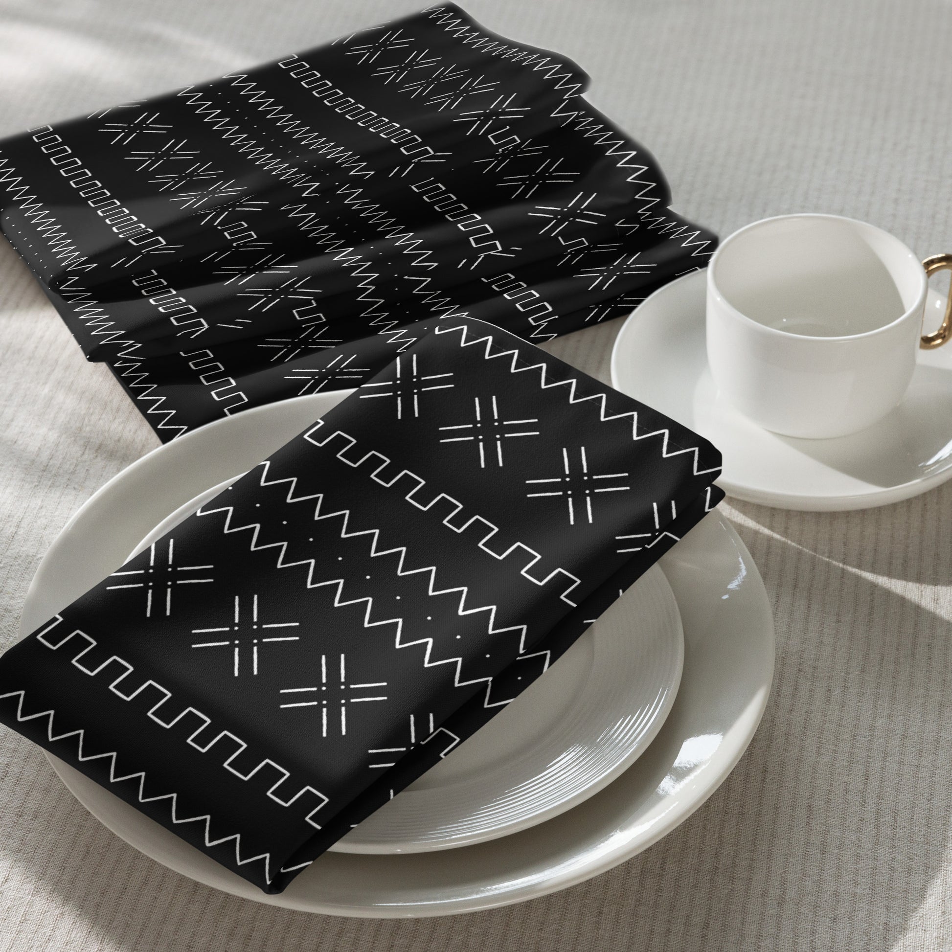 Black mudcloth patterned napkins on a white plate with a white cup and saucer.
