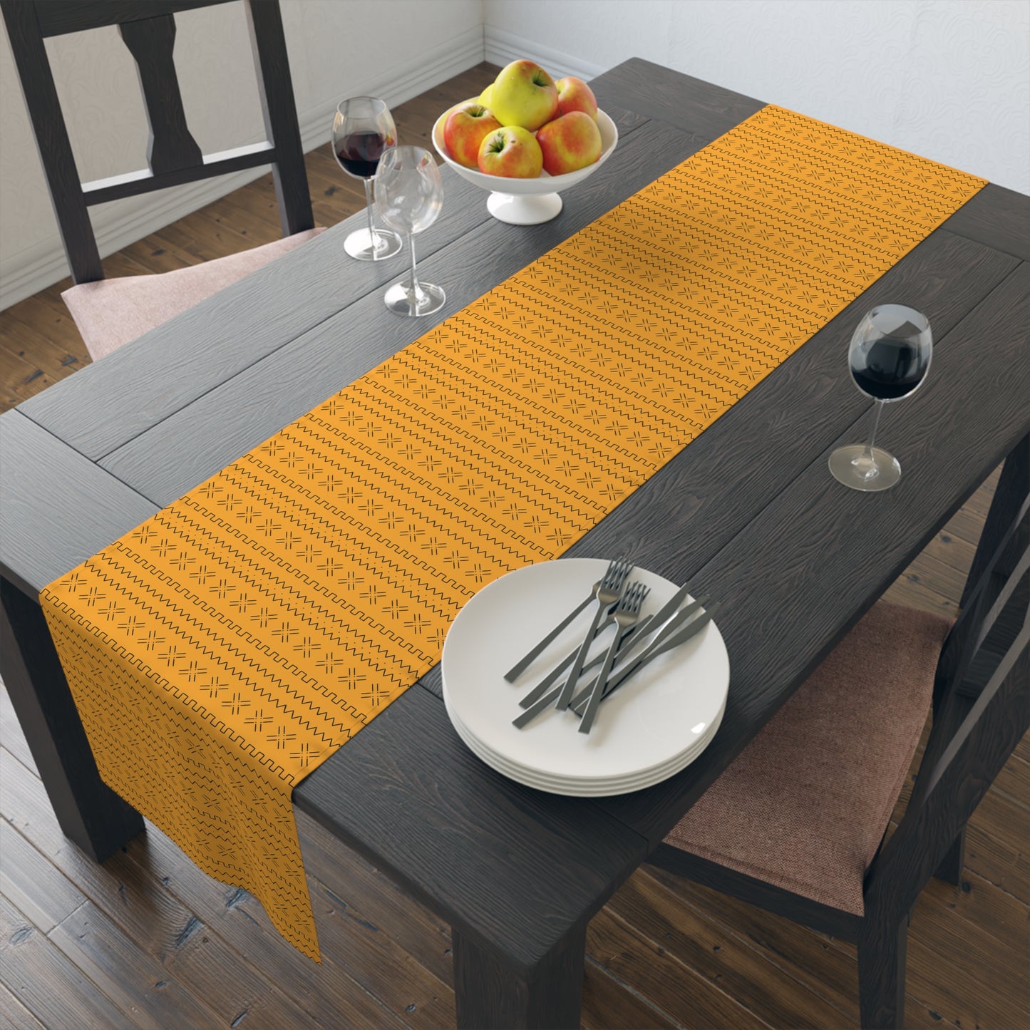 A yellow table runner with geometric mudcloth print laid out on a dining table with place settings and decorative flowers.
