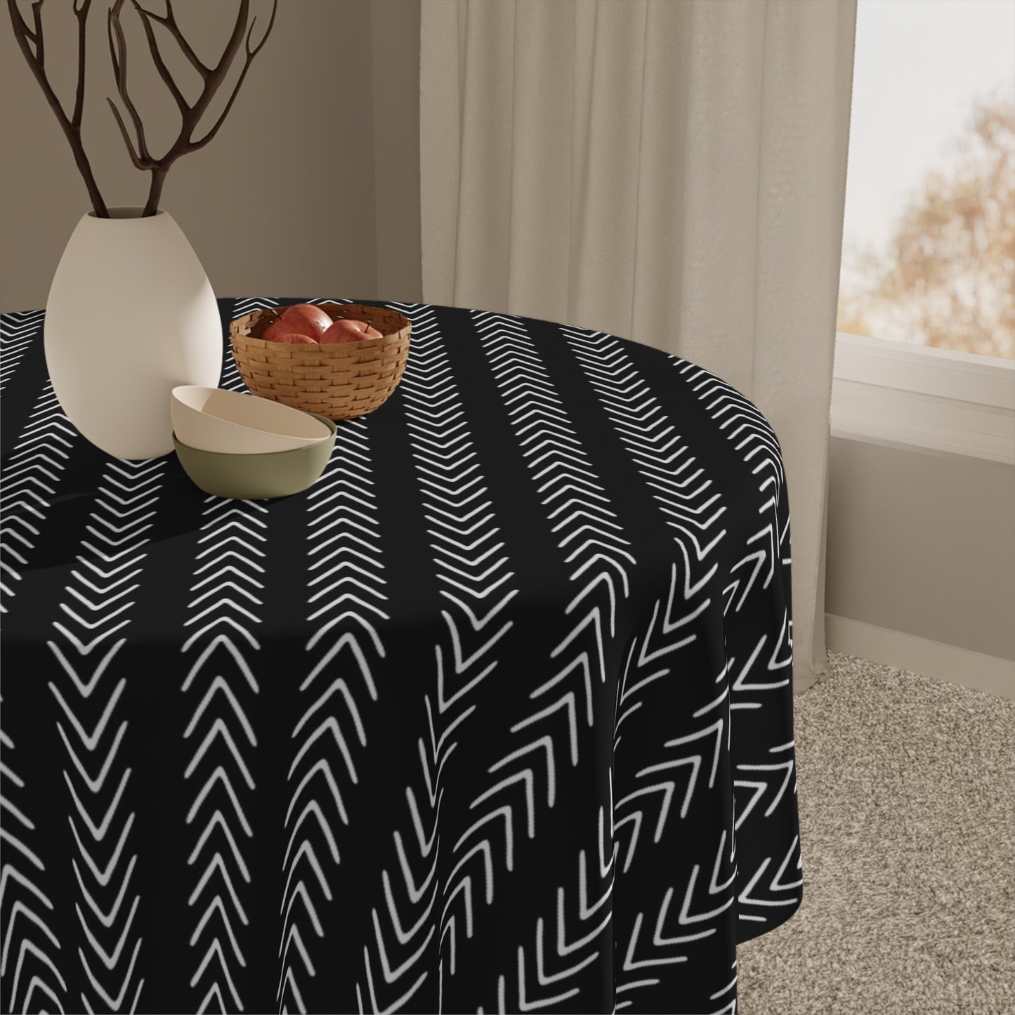 Table with a black and white zigzag patterned tablecloth in a room with a window and curtains.