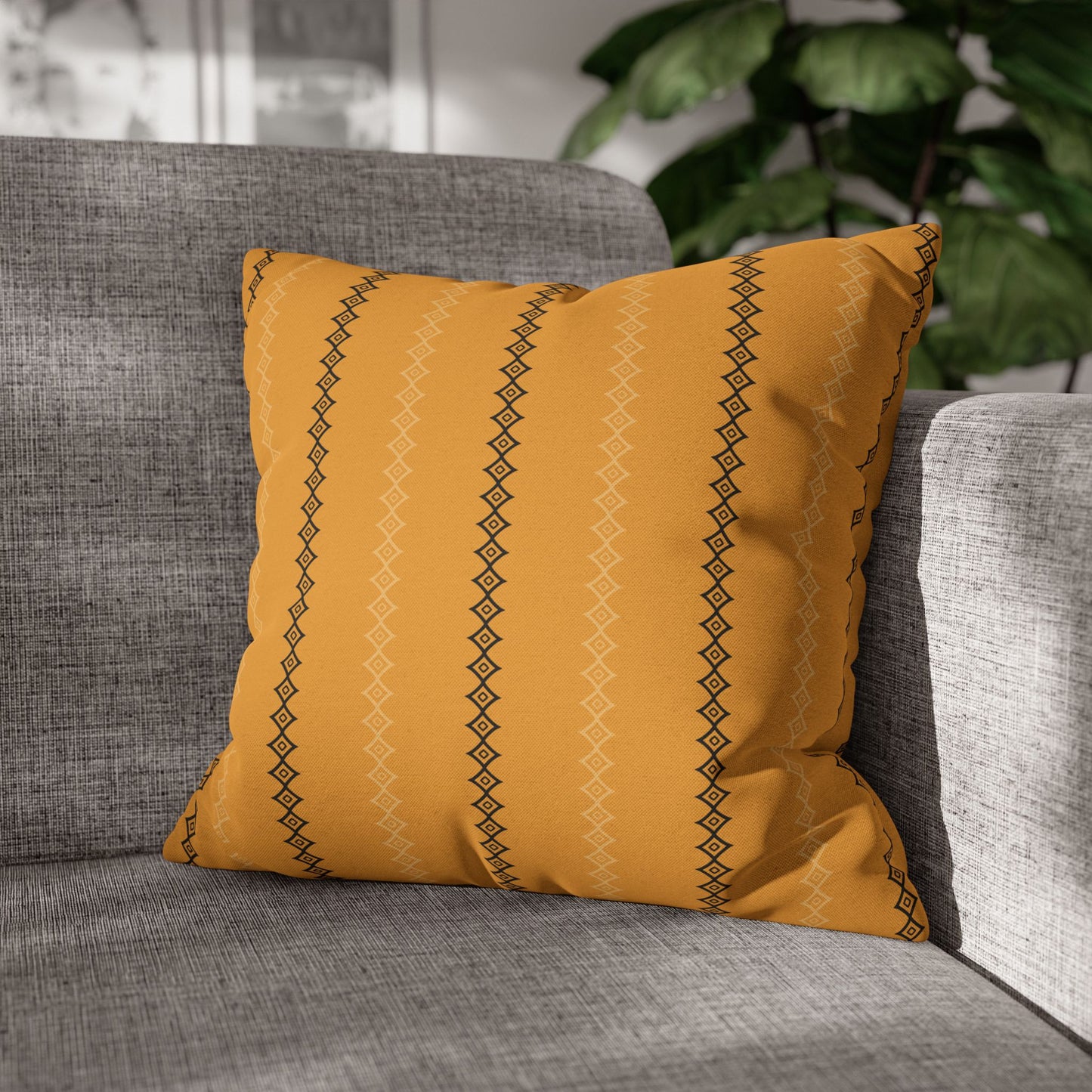 A gold mudcloth print throw pillow with black geometric patterns on a gray sofa.