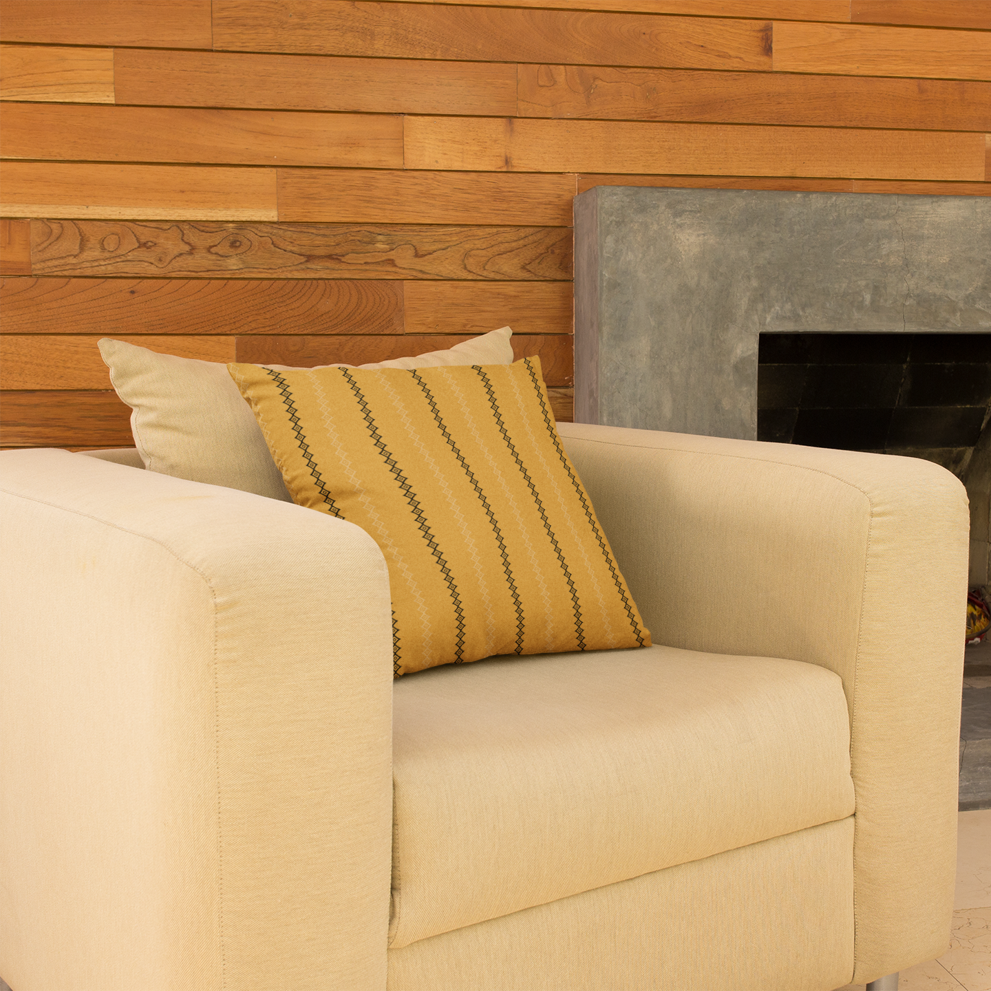 Beige armchair with a yellow gold mudcloth pillow in front of a stone fireplace.