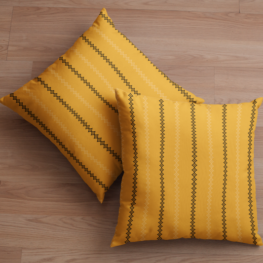 Two yellow gold mudcloth pillows with black stripes on a wooden floor.