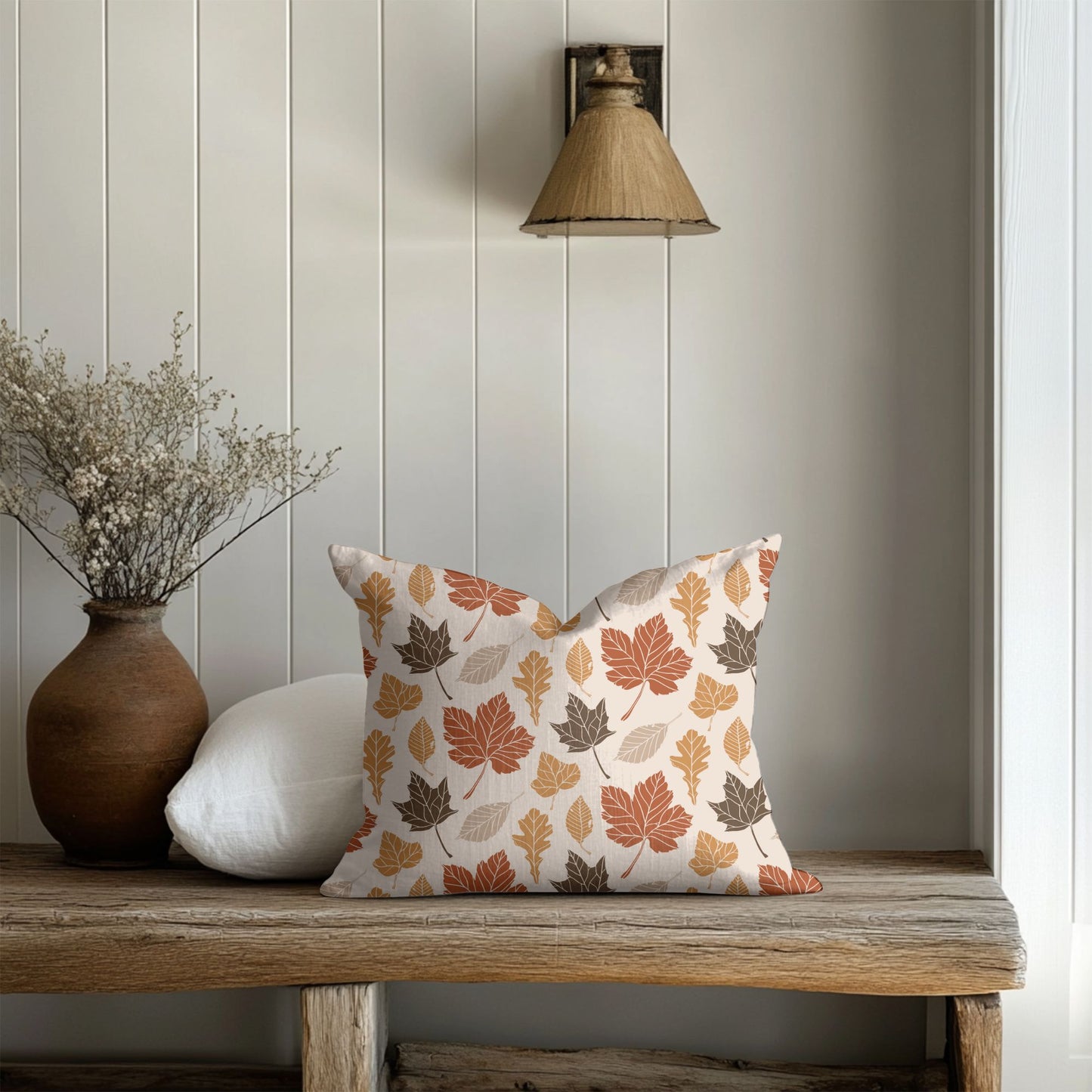 Decorative pillow with autumn leaf pattern on a wooden bench against a light paneled wall.