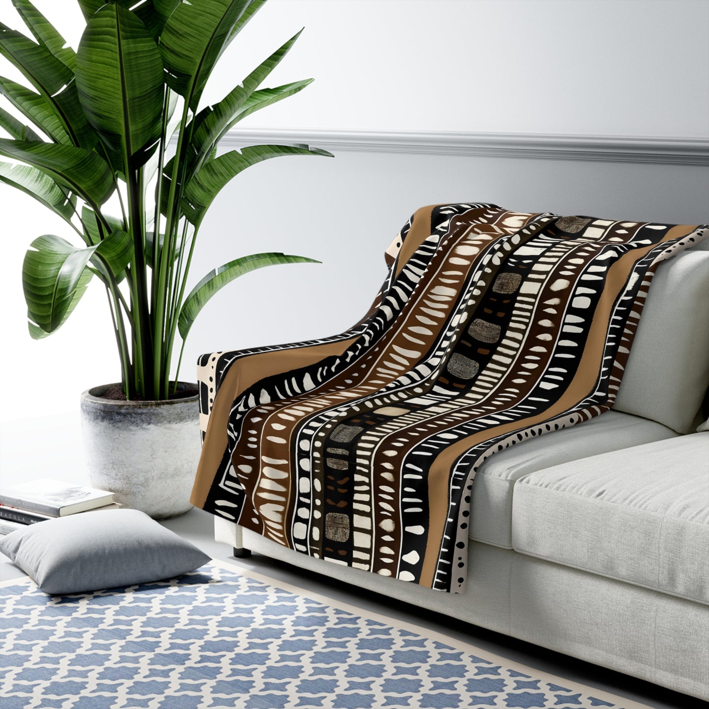 Patterned blanket draped over a sofa in a living room with a plant and rug.