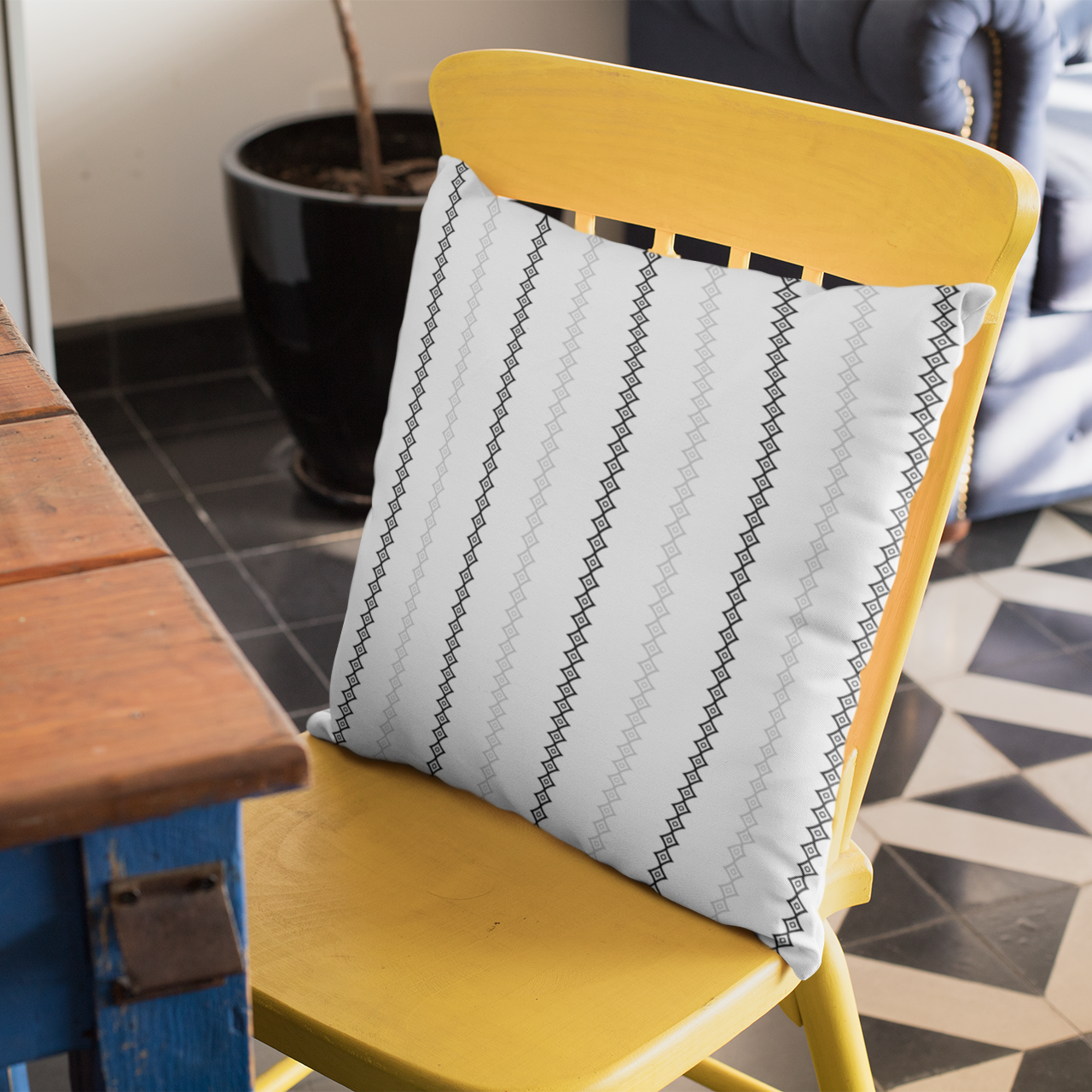 Yellow chair with a white mudcloth patterned cushion next to a wooden table on a tiled floor.